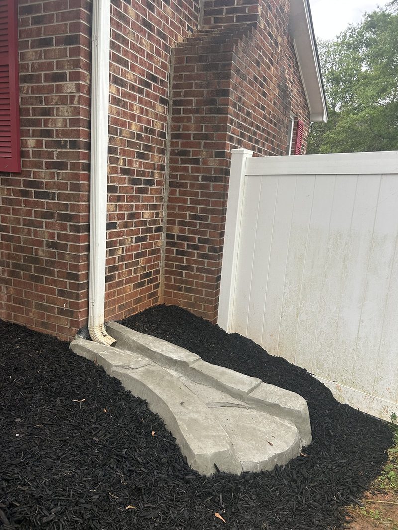 Custom concrete splash block for downspout drainage at brick home in Spartanburg SC