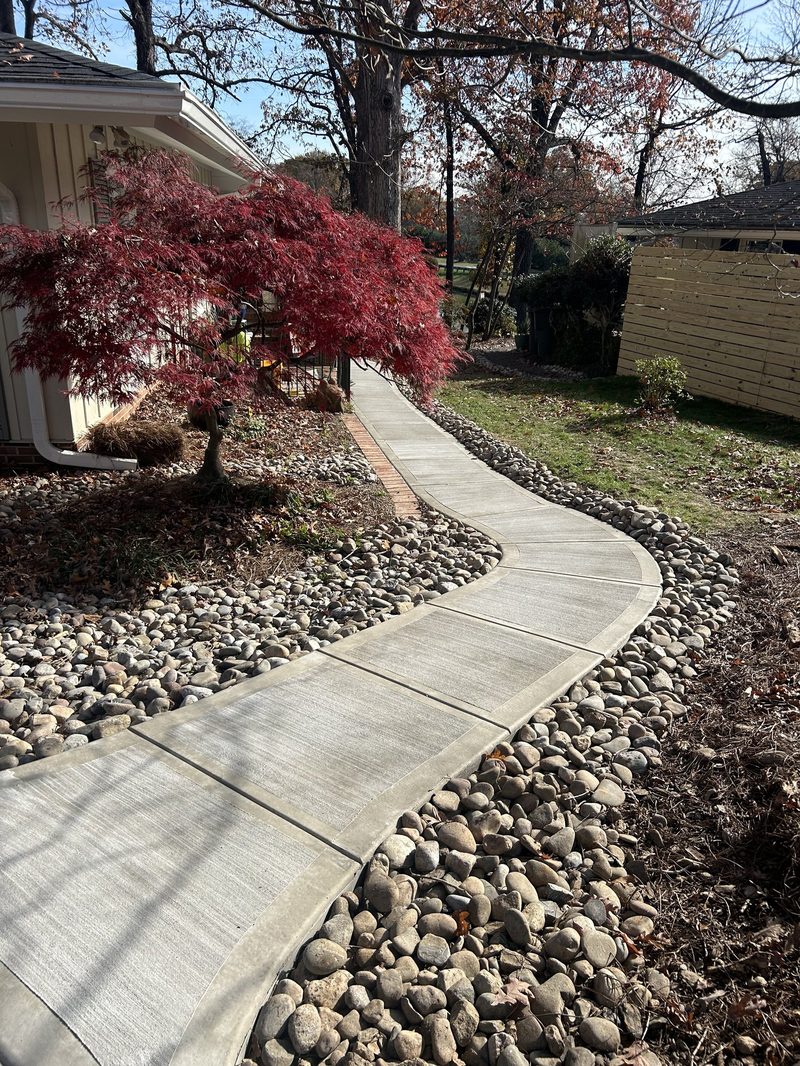 Curved concrete sidewalk with broom finish and river rock borders in Spartanburg SC
